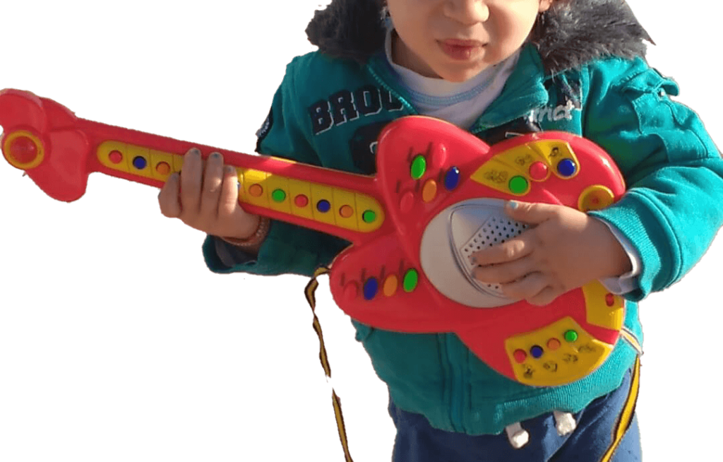 mi hijo menor con 2 años, caminando por la calle con una guitarra electrica de juguete. Se ven sus uñas pintadas de azul.