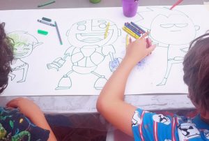 mis hijos de 5 y 7 años, de espaldas, sentados en la mesa mientras pintan un dibujo de los teen titans go que les dibujé sobre papel continuo