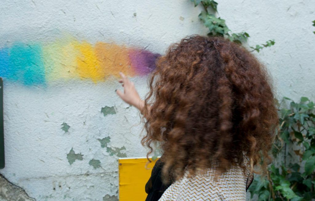 Geraldine de espaldas, señalando un arcoiris pintado sobre una pared blanca