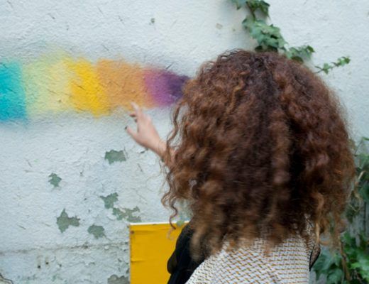 Geraldine de espaldas, señalando un arcoiris pintado sobre una pared blanca