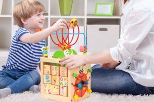 madre e hijo en el suelo jugando con un juguete con forma de cubo de madera con diferentes actividades de motricidad fina