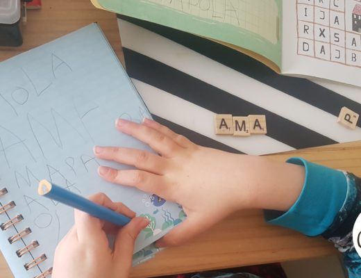 mi hijo de 6 años escribiendo en un cuaderno con un lapiz, a su lado unas letras de scrabble de ,adera con la palabra AMA. logo de criando 24/7