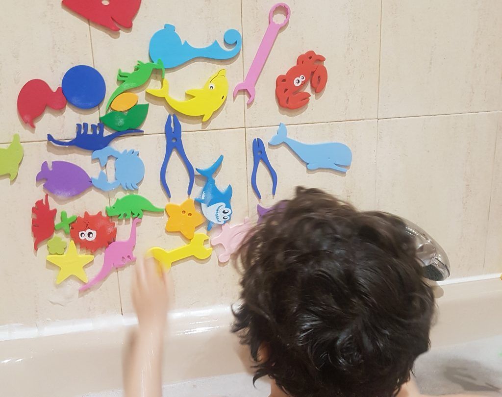 mi hijo de 6 años colocando figuras de goma eva en los azulejos de la pared sobre la bañera