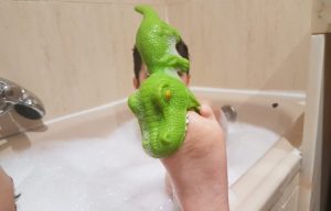 mi hijo de 6 años en la bañera, cubierto de espuma, con su pie en alto y un cocodrilo de goma encajado en sus dedos como si lo estuviese mordiendo