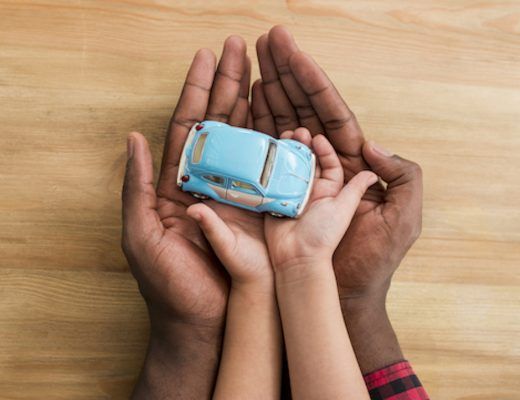 manos de un hombre palmas arriba, sosteniendo las de un niño que sujeta un coche de juguete