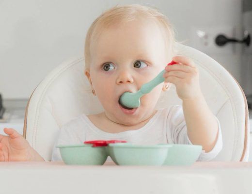 bebé rubio sentado en una trona comiendo con una cuchara