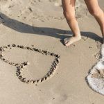pies de un niño al lado de un corazón dibujado en la arena, en la orilla del mar