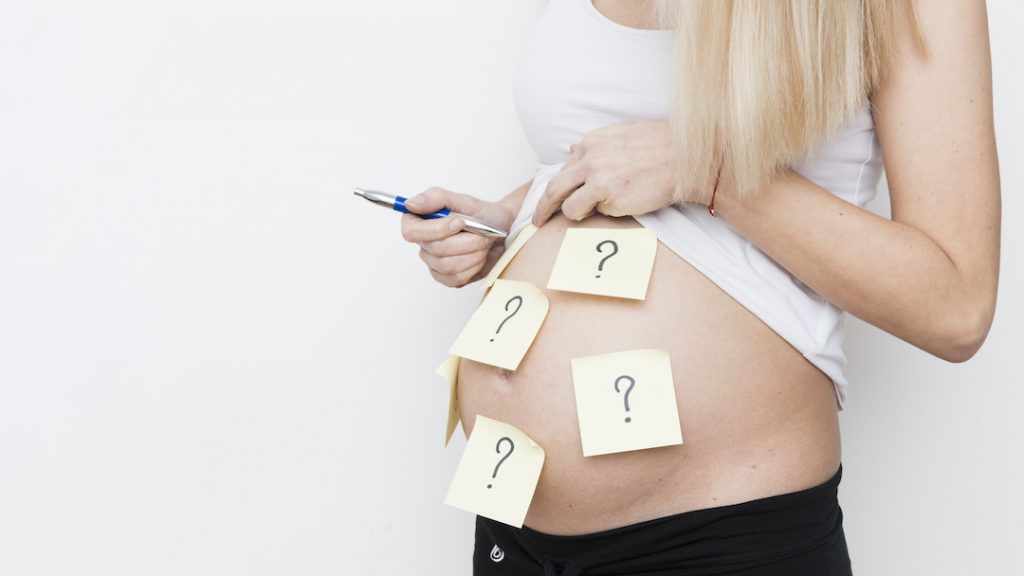 mujer embarazada con post its pegados en la tripa con signos de pregunta