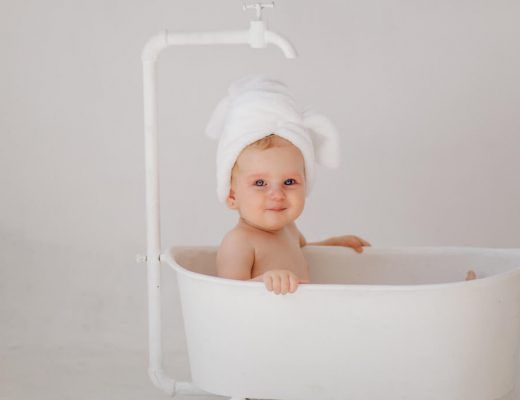 bebé sentada en una bañera blanca, con una toalla en la cabeza, sonriendo