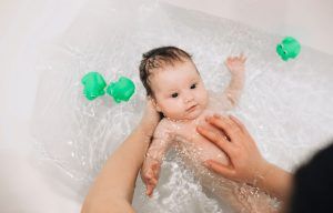 bebé en una bañera, sostenido por las manos de su madre