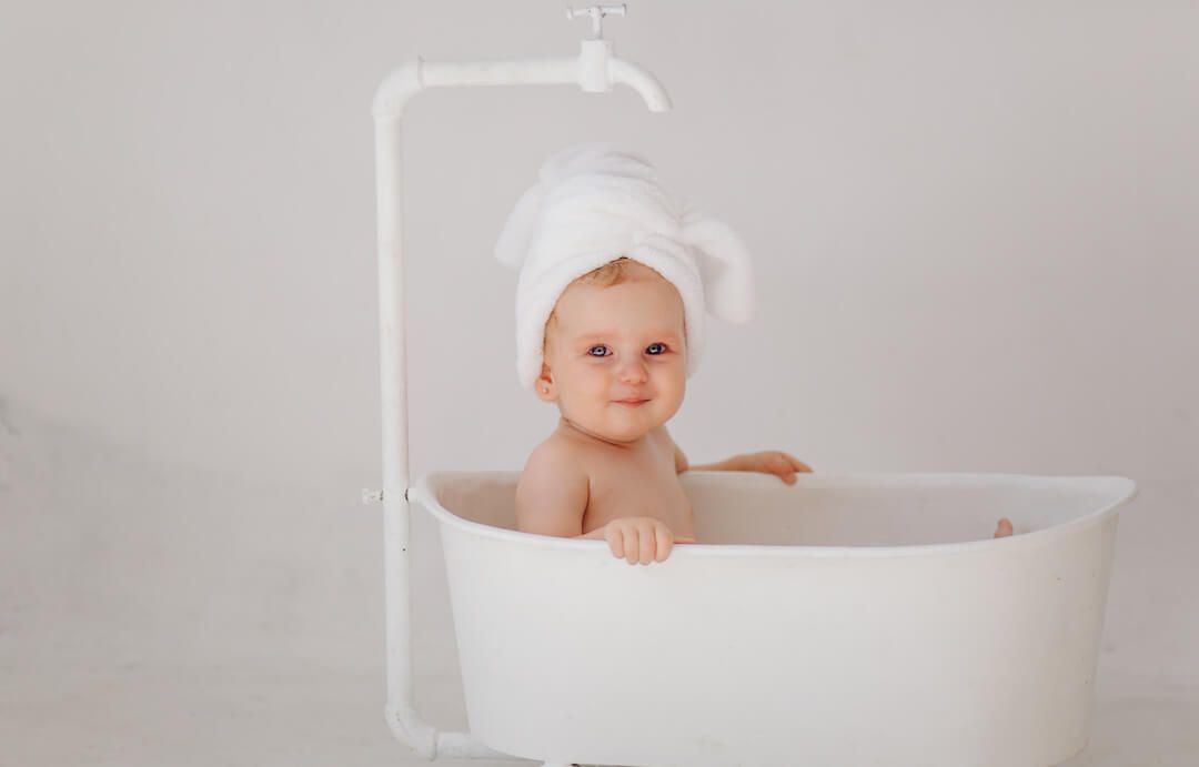 bebé sentada en una bañera blanca, con una toalla en la cabeza, sonriendo