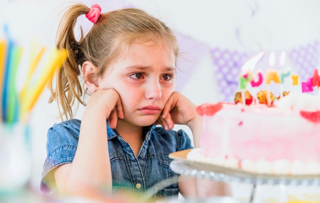 niña triste mirando a su tarta de cumpleaños