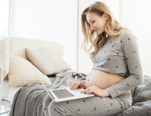 mujer embarazada sentada en el sofa mirando la pantalla de su portatil mientras sonríe