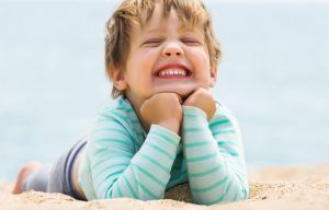 niño sonriendo recostado en la playa sobre la arena, con el mar de fondo