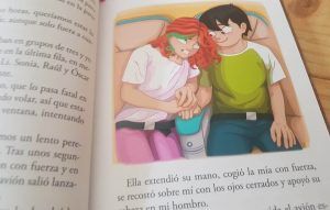 interior del libro de Txano y Oscar, con una ilustración de su protagonista sentado en el avión junto a su amiga Esmeralda, que le da la mano mientras él la mira sonriendo