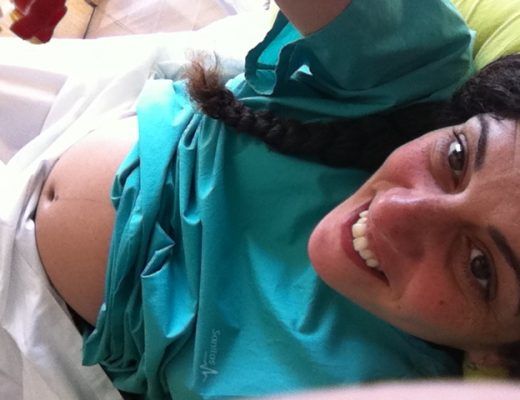 selfie recostada en una cama de hospital, con bata verde desde la que asoma mi tripa de 33 semanas, mientras sonrío