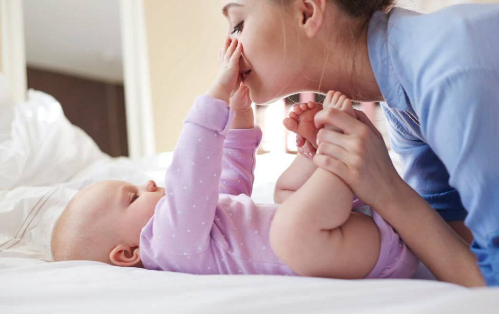mujer cogiendo los pies de un bebé recostado que la mira y le toca la cara con sus manitas