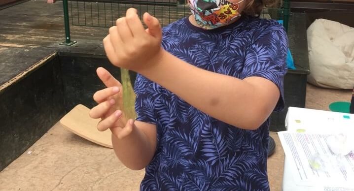 mi hijo de 9 años, de pie, pasando un slime amarillo de una mano a otra