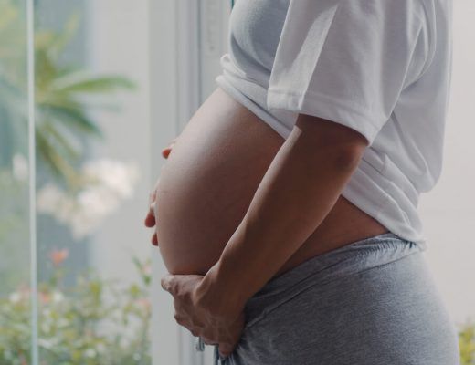mujer embarazada cogiéndose la tripa frente a un ventanal donde se ven plantas.