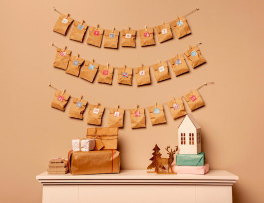 foto de un calendario de adviento de bolsas de papel kraft colgadas en tres lineas de cuerdas, sobre un recibidor con decoraciones navideñas