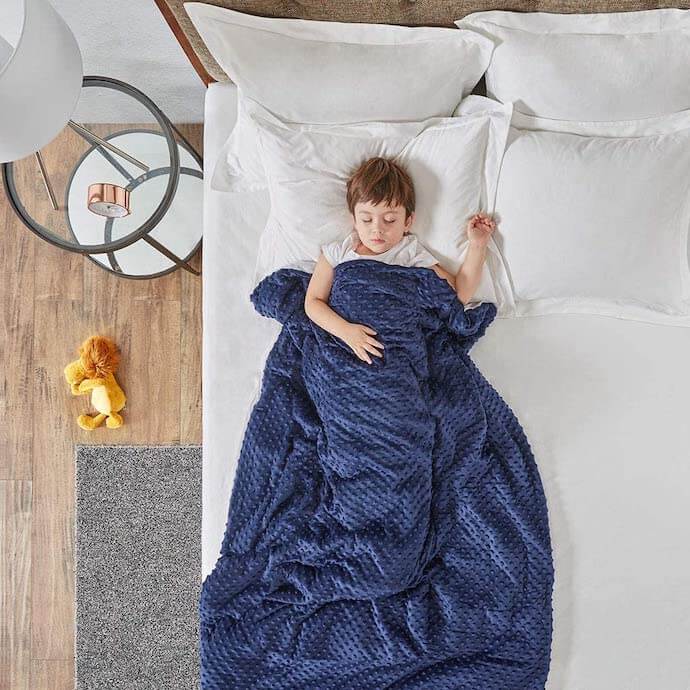 nilo durmiendo en una cama con una manta ponderada azul 