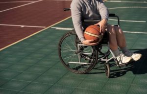 chico en silla de ruedas en pista de bañoncesto con una pelota en las manos