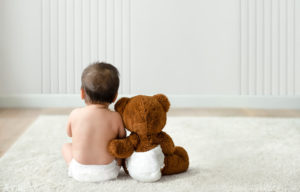 bebe sentado en pañales, al lado de un oso de peluche
