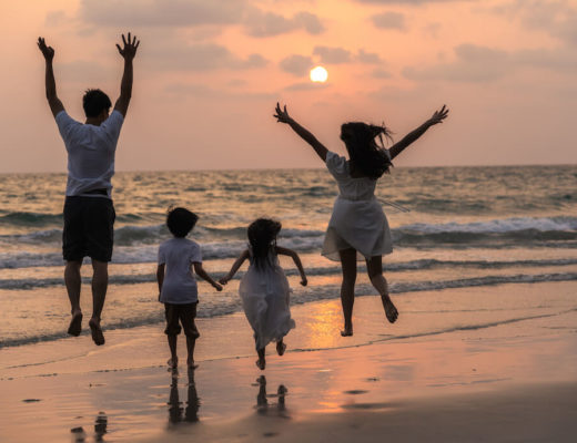 familia de 4, padre madre niño y niña, de espaldas, saltando en la orilla de la playa al atardecer