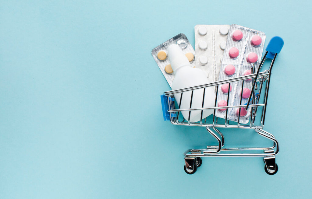 foto de un carro de la compra con blisters de pastillas de medicamentos. fondo azul