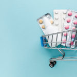 foto de un carro de la compra con blisters de pastillas de medicamentos. fondo azul