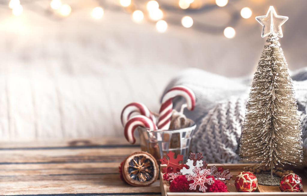 decoración navideña: un arbolito pequeño, al lado de un vaso de cristal con bastones de caramelo rojos y blancos. Detrás se ve una alfombra mullida color crema y guirnaldas de luces cálidas