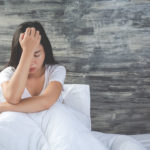 mujer en la cama, sentada, apoyando la cabeza en su mano con gesto de agotamiento