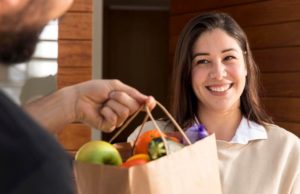 mujer sonrie mientras un mensajero le entrega una bolsa de la compra