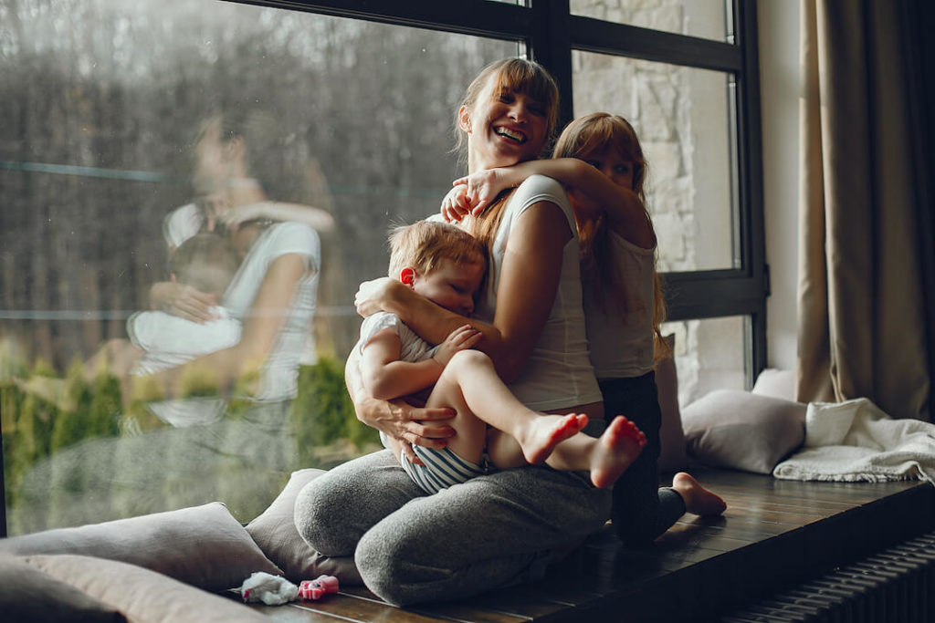 mujer en una ventana con dos niños abrazándola