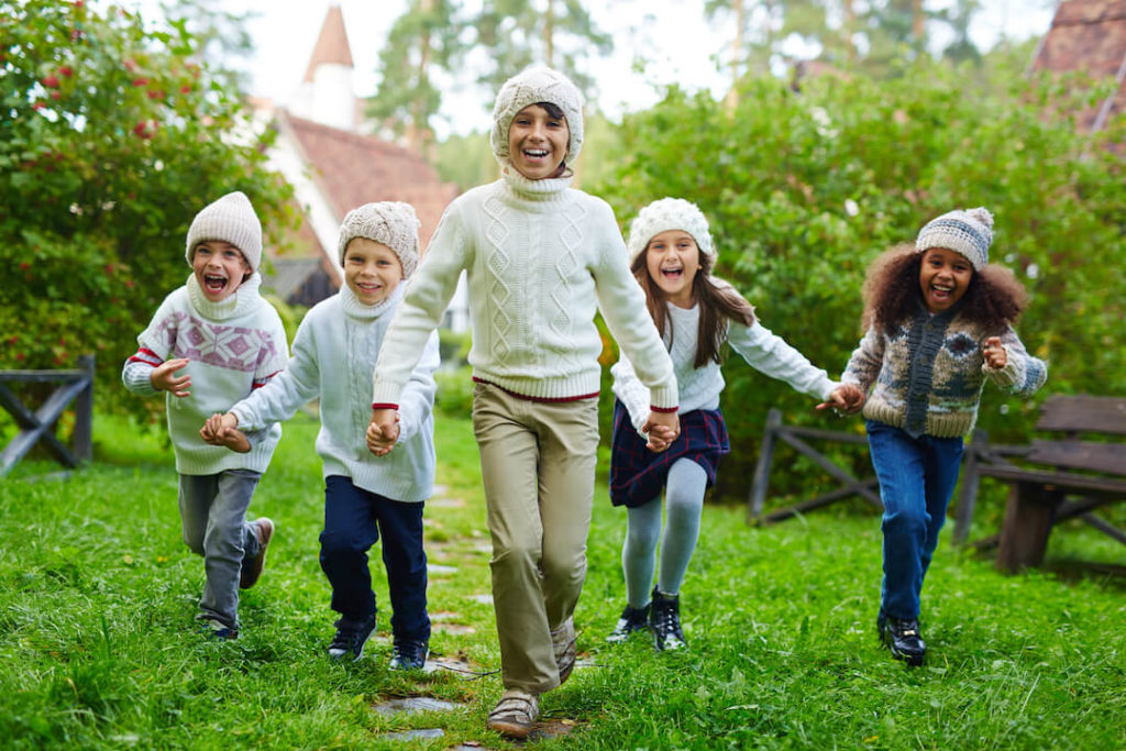 grupo de niños y niñas corriendo por un jardín, sonriendo, vestidos de invierno
