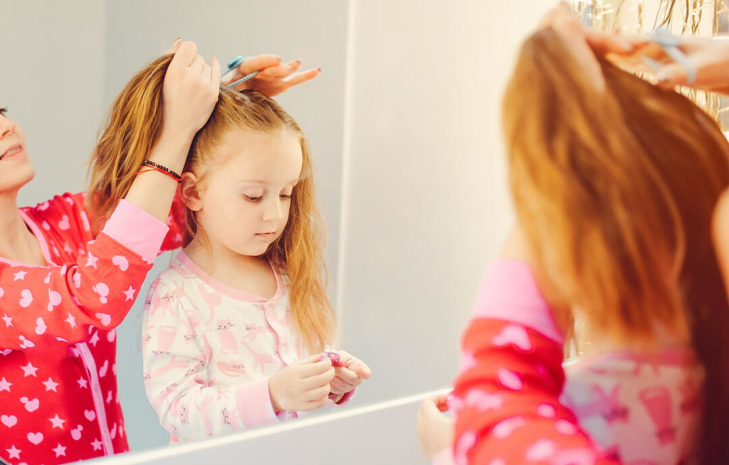 niña con melena larga pelirroja frente al espejo mientras la peinan
