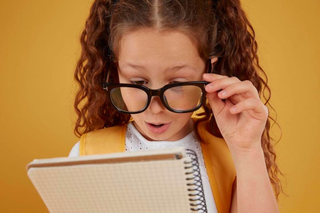 niña con gafas mira sorprendida un bloc de notas