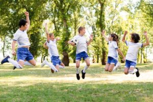 grupo de niños y niñas con ropa de futbol saltando en un parque mientras sonríen