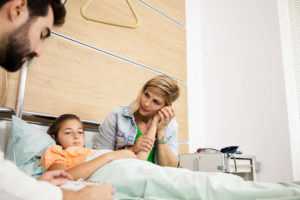 madre acaricia la mano de su hija, recostada en una cama de hospital, con el médico a su lado