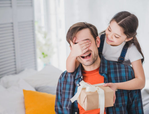 niña tapa los ojos del padre mientras le da un regalo