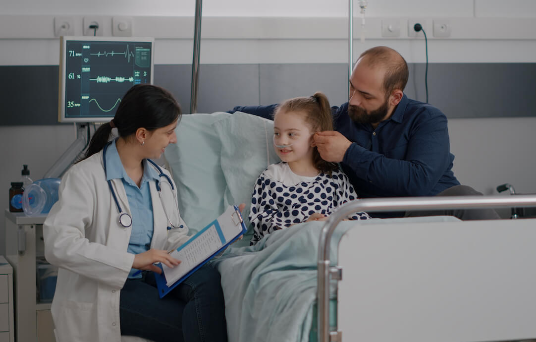 foto de un padre con su hija en una cama de hospital, al lado de una médico, en relación al requisito de hospitalizacion de la prestacion CUME