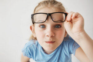 foto de una niña rubia con coleta mirando a cámara, mientras sujeta sus gafas por encima de sus ojos