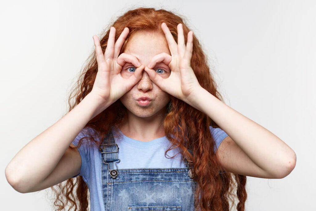foto de una adolescente pelirroja haciendo un signo de gafas con sus manos sobre los ojos