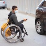hombre joven sentado en una silla de ruedas abriendo un coche con la llave a distancia