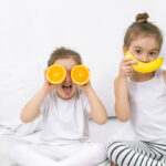 fotos de dos niñas sentadas en una cama con naranjas y un plátano